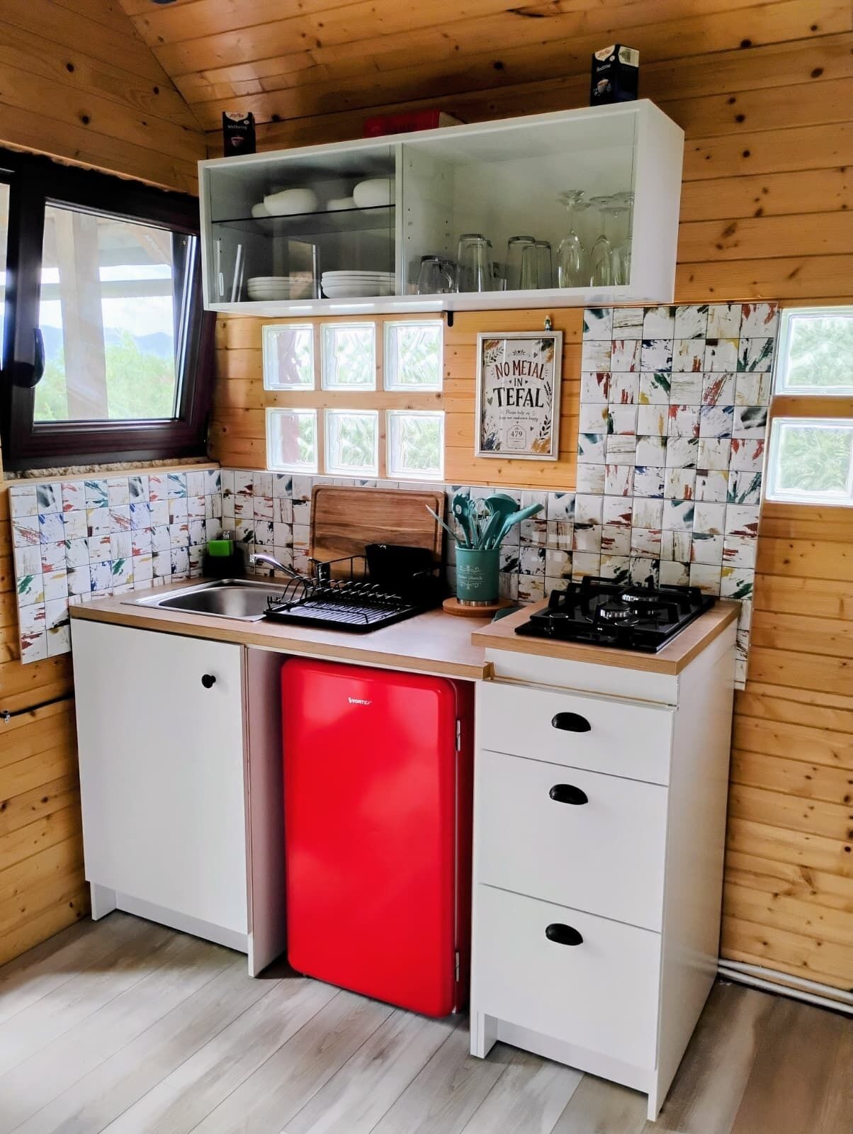 Una cocina compacta con lavavajillas rojo, armarios blancos y salpicadero de azulejos.