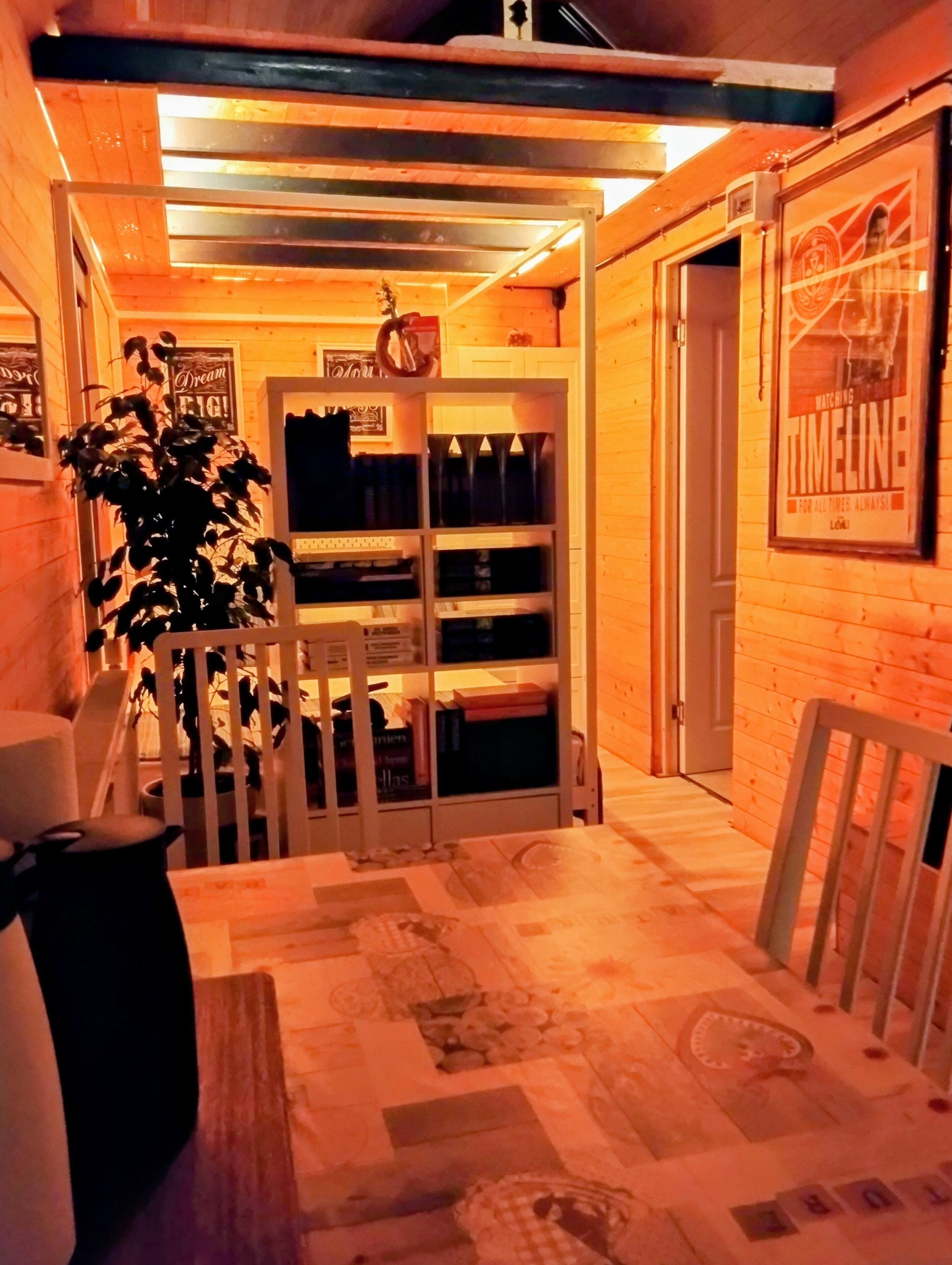 Une pièce chaleureuse avec un plancher en bois, une petite table, une chaise, une étagère remplie de livres et une porte.