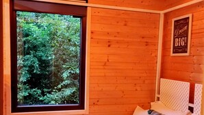 A wooden room with a bed, a window with a view of greenery, and a 'Dream BIG!' sign on the wall.
