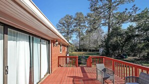 A wooden deck with outdoor furniture, a glass door, and a view of a grassy yard and trees. - Marietta 2BR Close to Atlanta! (Marietta)