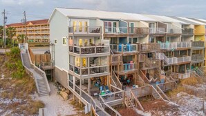 Ett flervåningshotell vid stranden med balkonger, utomhusmöbler och en träbrygga.