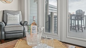 Ett rum med en grå fåtölj, ett stort fönster med persienner, en flaska ”YES WAY ROSE” i en genomskinlig isspand och tre glas på en vävd underlägg.