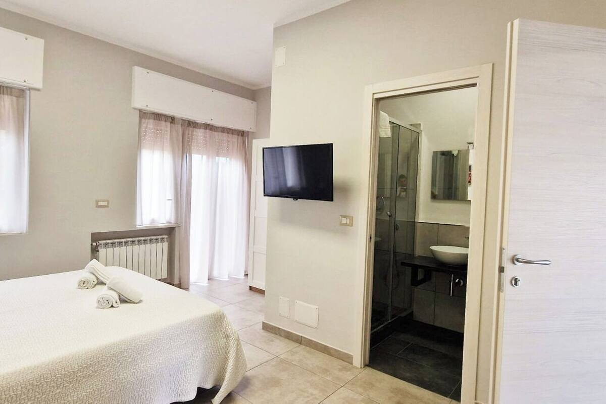 A hotel room with a bed, a television, a bathroom with a sink, and a door leading to another room.