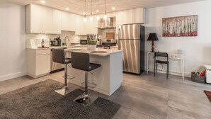 Une cuisine moderne avec des meubles blancs, un îlot central doté de tabourets, des appareils en acier inoxydable et un luminaire suspendu.