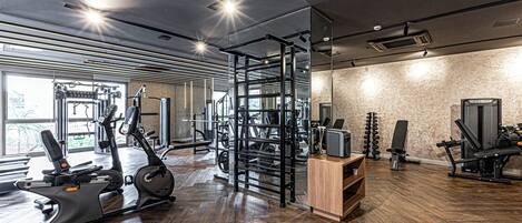A gym with exercise equipment, wooden flooring, and large windows.