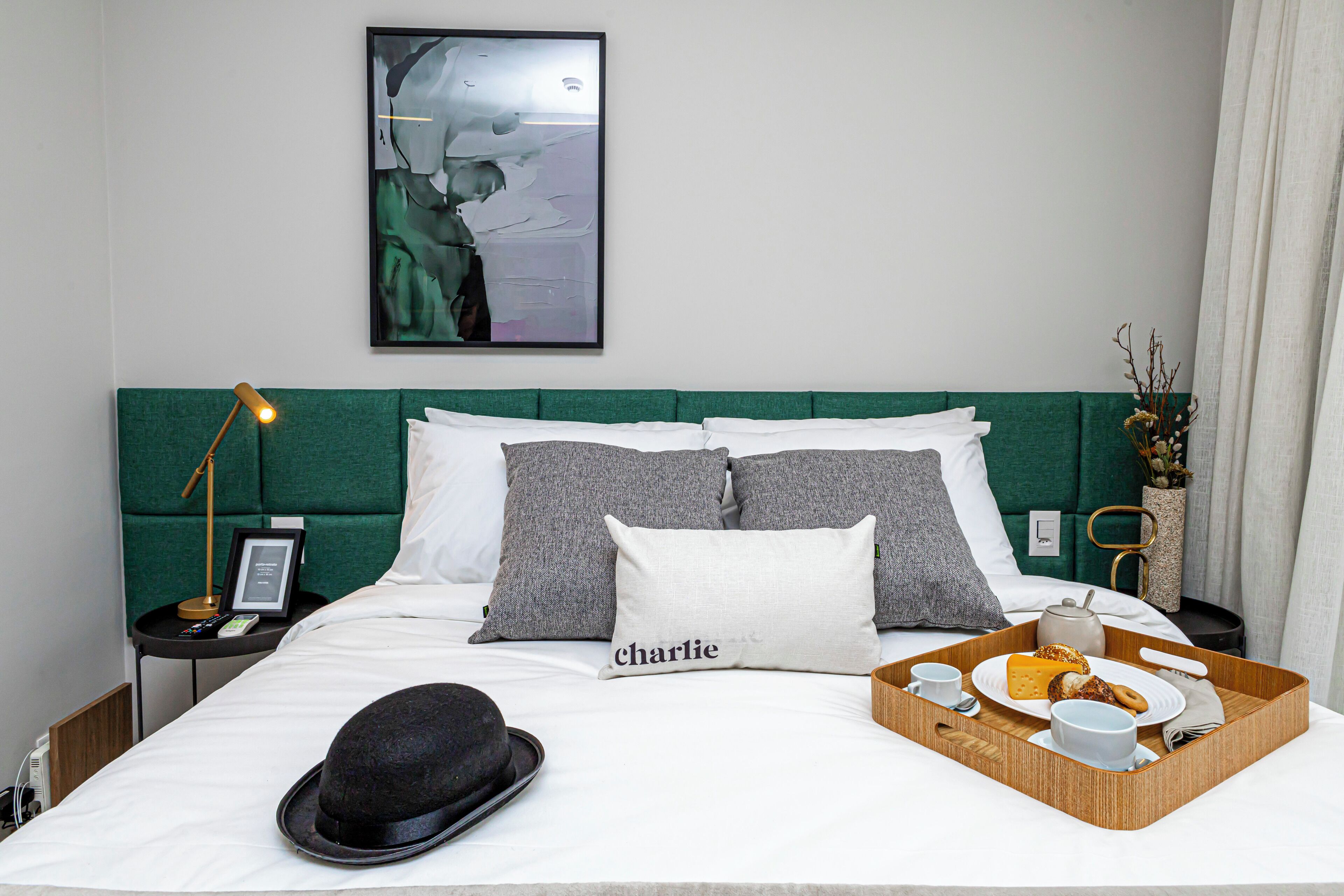 A neatly made bed with a tray of breakfast items, a black hat, and a pillow with the name "Charlie".