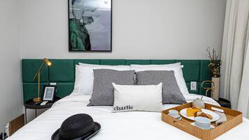A neatly made bed with a tray of breakfast items, a black hat, and a pillow with the name "Charlie".