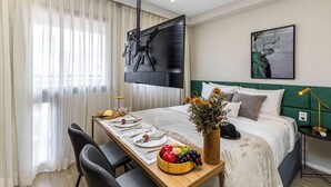 A neatly arranged hotel room with a bed, a dining table set for two, a television mounted on the wall, and a painting above the bed. - Charlie Atmosfera Santo Amaro (São Paulo)