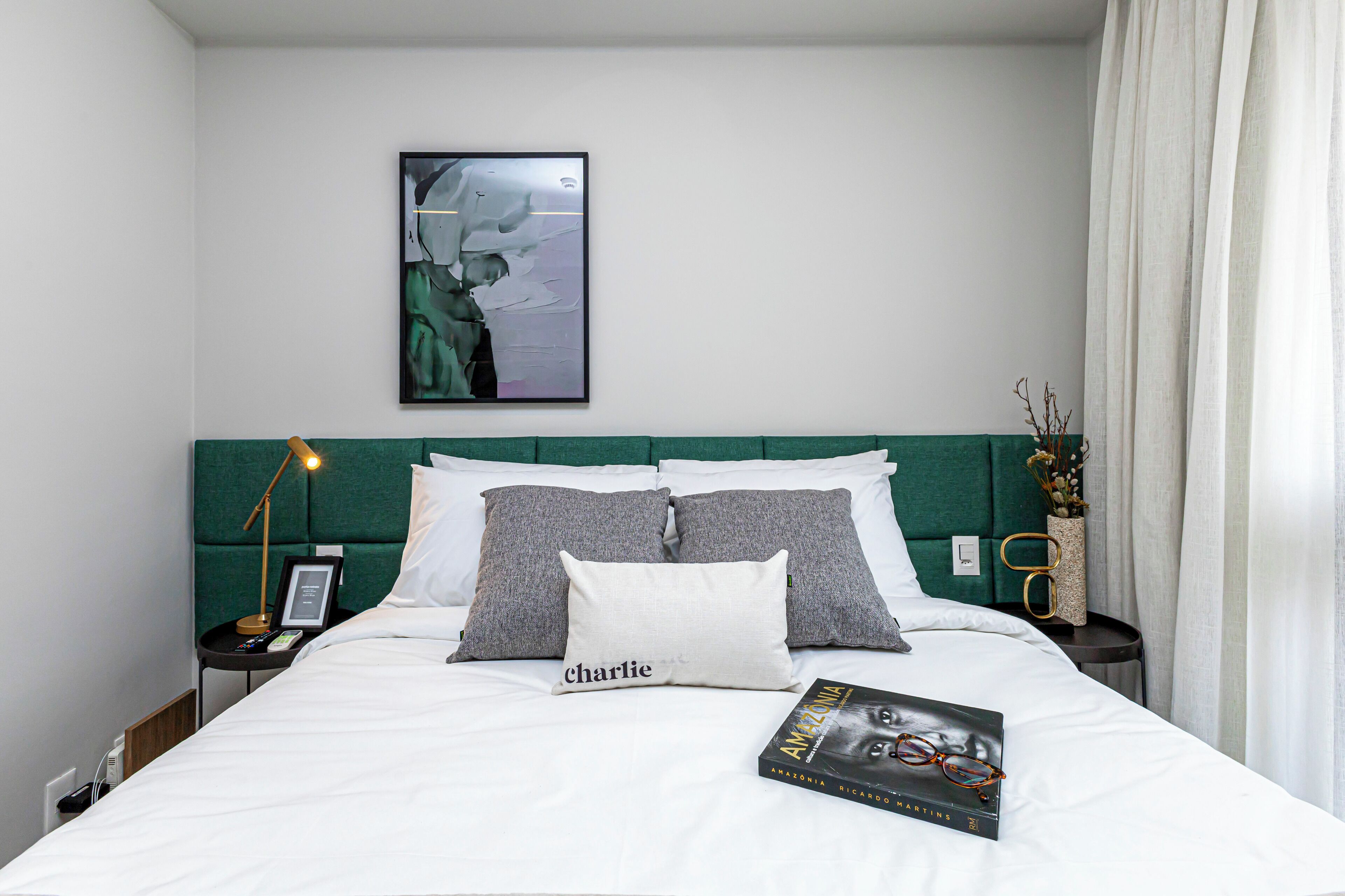 Un lit bien fait, avec un oreiller sur lequel est écrit le mot « Charlie », un tableau accroché au mur et un livre intitulé « AMAZONIE » posé sur le lit.