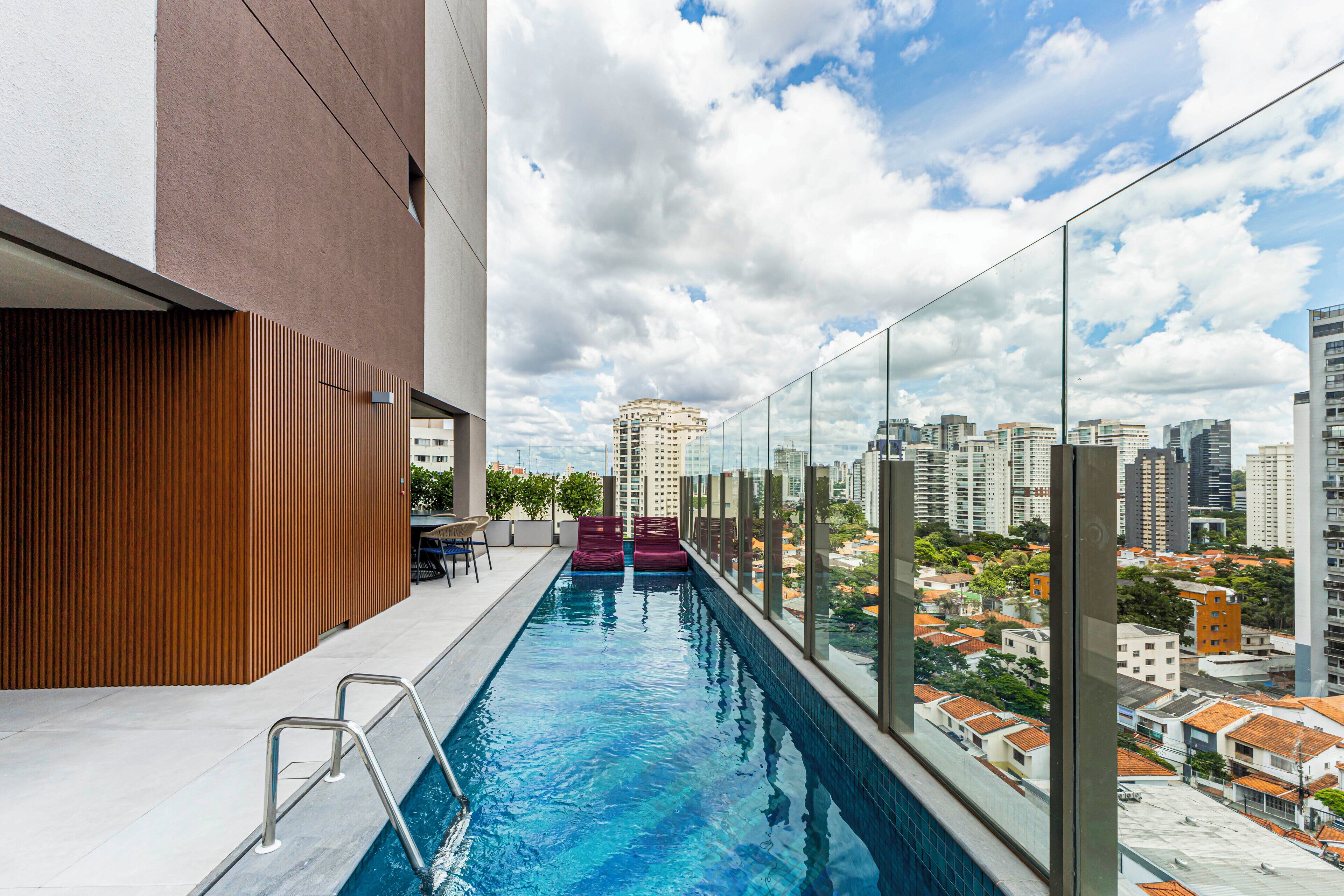 A rooftop pool with a glass railing, a wooden wall, and a city view.