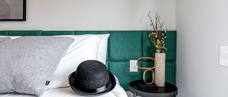 A neatly made bed with white and gray pillows, a black hat, and a vase with flowers on a bedside table.