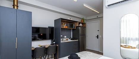 Ett kompakt hotellrum med ett litet kök, en säng med ett brickbord med frukost, en spegel och en tv.