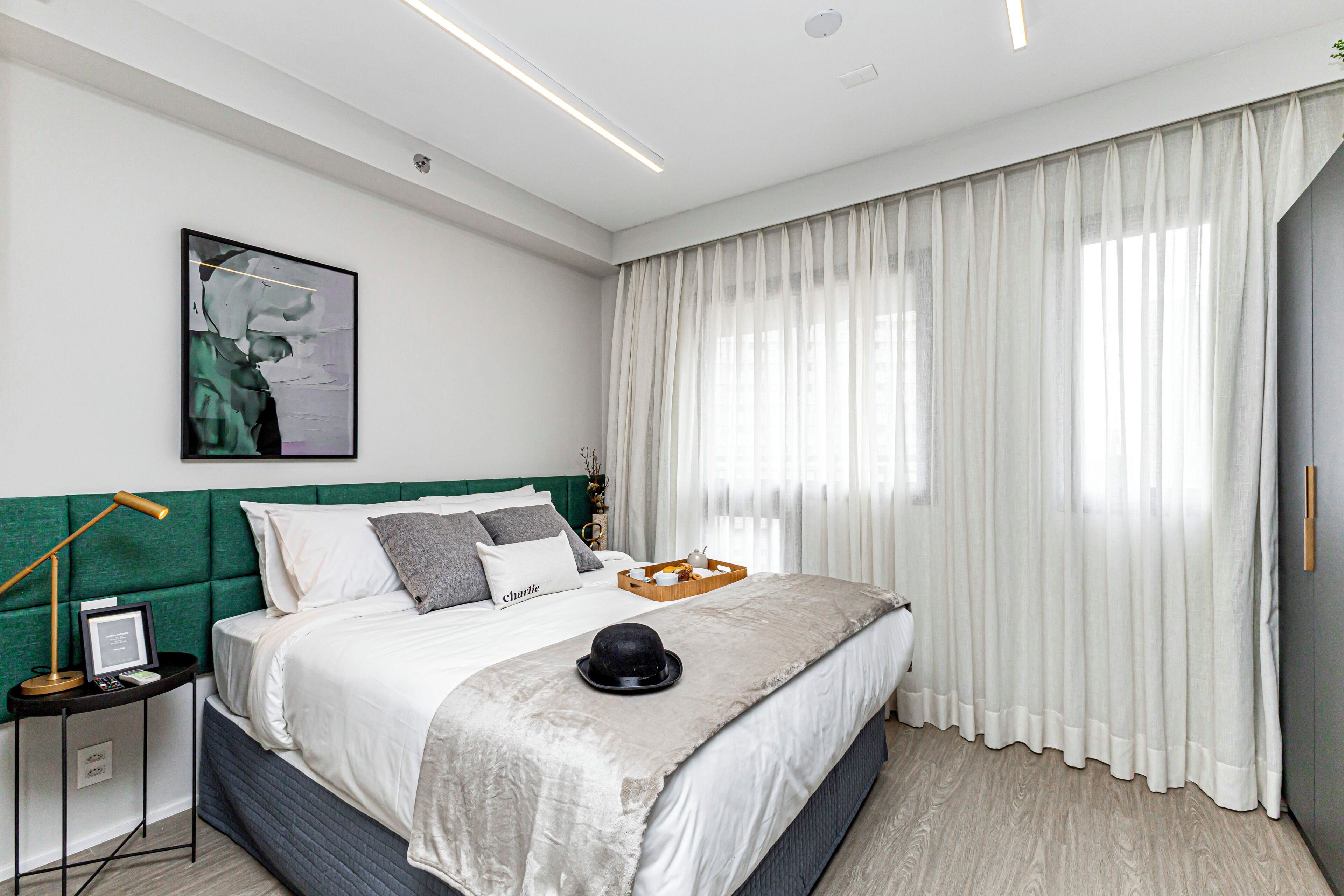 Une chambre moderne avec une tête de lit verte, un grand lit avec une literie blanche, une table de chevet avec une lampe et un tableau encadré au mur.