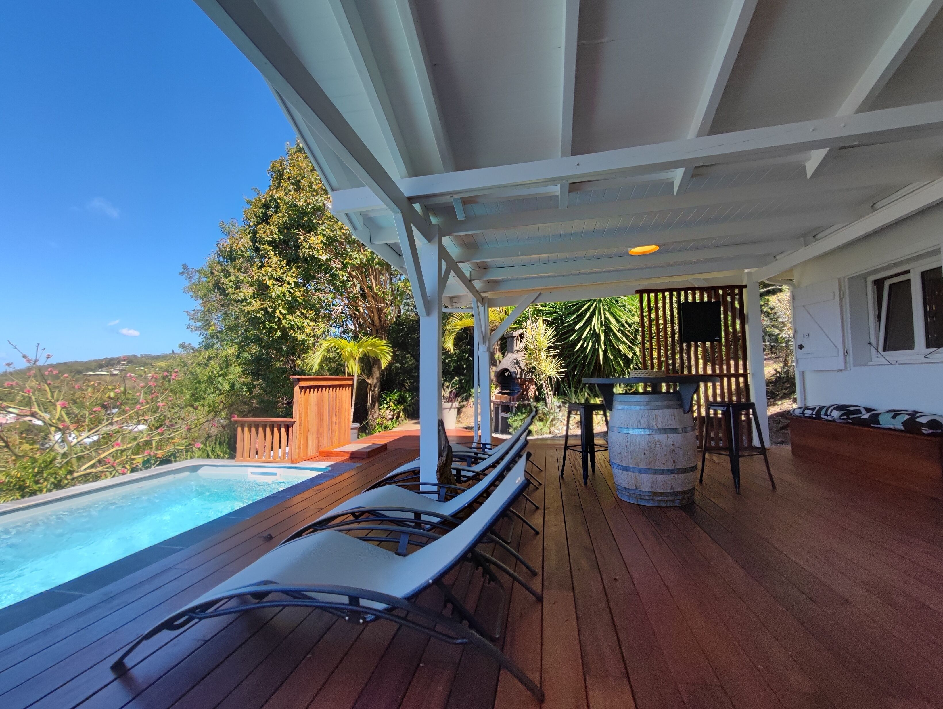 A covered outdoor area with a pool, lounge chairs, a wooden deck, and a bar area.