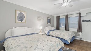 Un dormitorio con dos camas, ventilador de techo y ventana con cortinas.