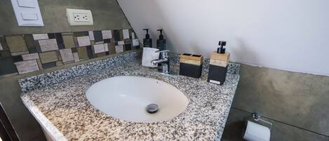 Un bagno con un piano di lavoro in granito, un lavandino bianco, un porta asciugamani e un porta carta igienica.