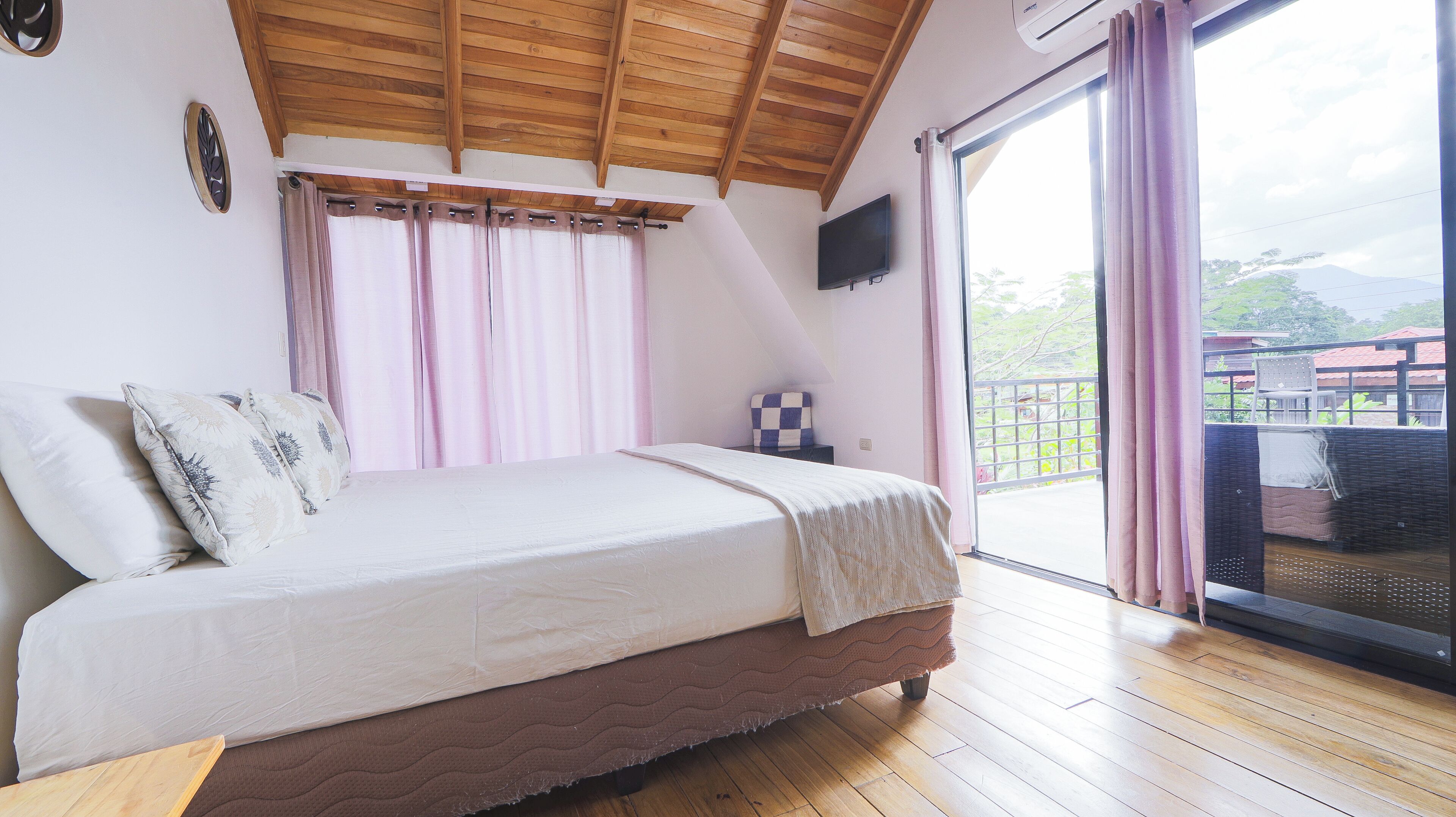 Ein Schlafzimmer mit Bett, Holzboden, Fernseher und Balkon mit Aussicht.