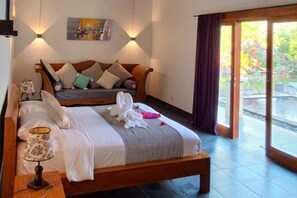 A bedroom with a bed, pillows, a lamp, a painting, and a view of a garden through a glass door. - Villa - Sleeps 6 - Private Pool - Parking (Karangasem)