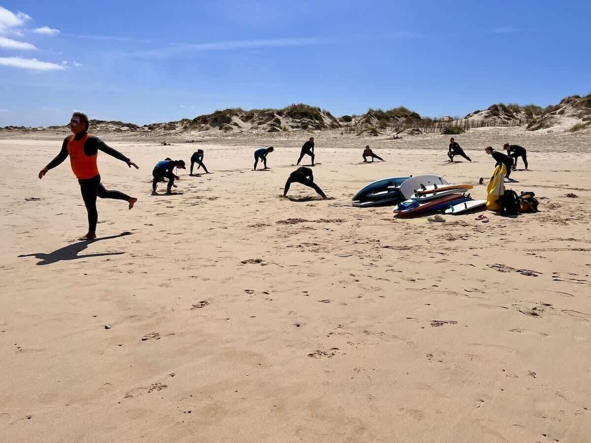 A sandy beach with people engaging in activities, some with surfboards and equipment.