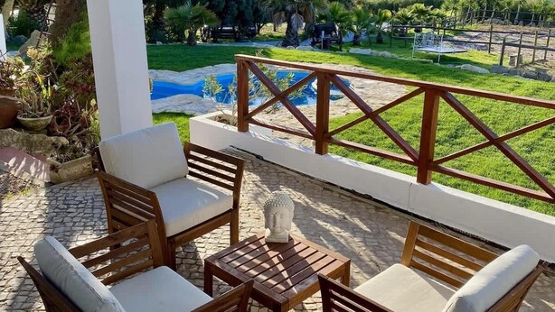 A patio with outdoor furniture, a stone table, and a view of a pool and greenery. - Da Silva Surfcamp Bedroom Abelheira for 3 persons (Lourinhã)