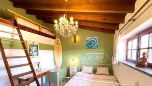 A bedroom with a bed, a wooden ladder, a chandelier, a surfboard, and a window. - Da Silva Surfcamp Bedroom Abelheira for 3 persons (Lourinhã)