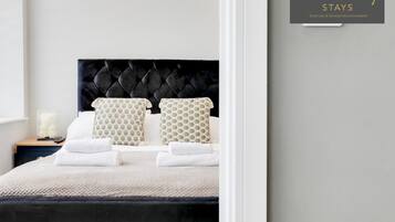 A neatly made bed with a black headboard, white bedding, and patterned pillows.