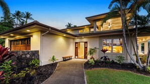 A modern house with a stone wall entrance, a covered patio, and a well-maintained garden.