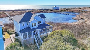 A large house with a dock extending into a body of water, surrounded by marshland. - The Loggerhead: Oceanfront, Beautiful Walkway Over Marsh (Oak Island)