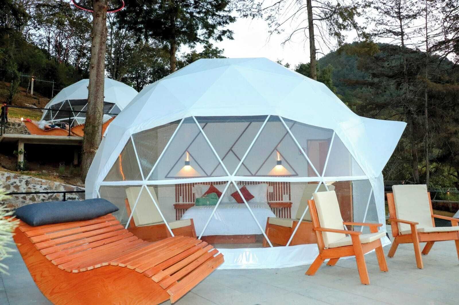 A geodesic dome structure with a central seating area, wooden benches, and chairs.