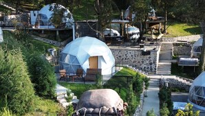 A resort with modern geodesic dome structures, a large sculpture of a figure with a mask, and a well-maintained garden path.