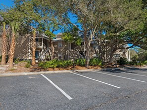 A parking lot with multiple parking spaces, a building with a balcony, and trees. - Near Pool, Playground, Walk to Beach (Miramar Beach)