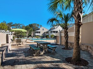 A pool area with lounge chairs, a table, and a palm tree. - Near Pool, Playground, Walk to Beach (Miramar Beach)