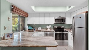 A modern kitchen with white cabinets, stainless steel appliances, and a large island with a marble countertop. - Near Pool, Playground, Walk to Beach (Miramar Beach)