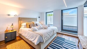 Ein modernes Schlafzimmer mit einem großen Bett, Nachttischlampen, einem Beistelltisch und Blick ins Freie durch ein großes Fenster.