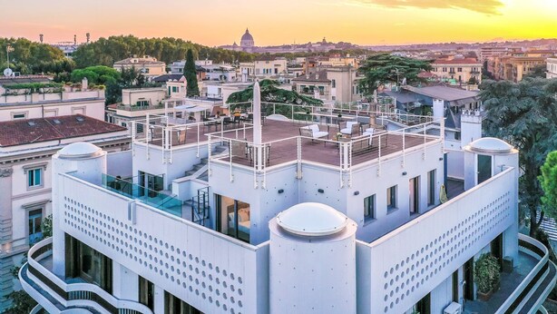 Ein modernes Gebäude mit Dachterrasse, großen Fenstern und einer Kuppel im Hintergrund.