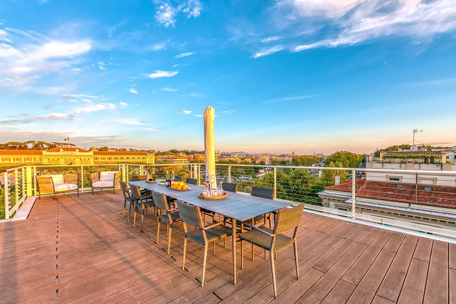 Eine Dachterrasse mit Tisch und Stühlen, einer Flagge und Blick auf Gebäude und Bäume.