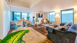 Ein modernes Wohnzimmer mit einer Couch, einem Essbereich mit Stühlen, einem Couchtisch und einem großen Fenster.