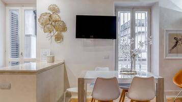 A modern kitchen with a central island, a dining area with two chairs, and a flat-screen TV mounted on the wall.