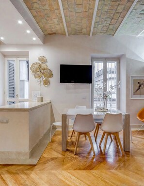 Een moderne keuken met een centraal eiland, een zithoek met twee stoelen en een flatscreen televisie aan de muur.