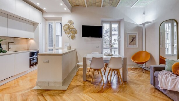 Una cocina moderna con armarios blancos, una isla central y un comedor con mesa y sillas.
