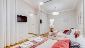 Un dormitorio moderno con un espejo grande, un televisor y una cama con ropa de cama rosa y roja.