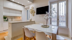 Una cocina moderna con armarios blancos, una isla central y un comedor con una mesa y sillas blancas.