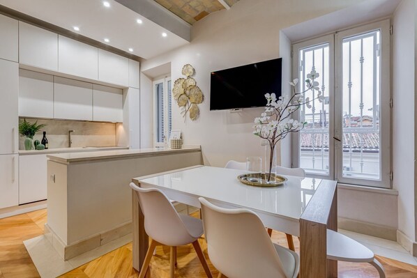 Une cuisine moderne avec des meubles blancs, un îlot central et un coin repas comprenant une table et des chaises blanches.