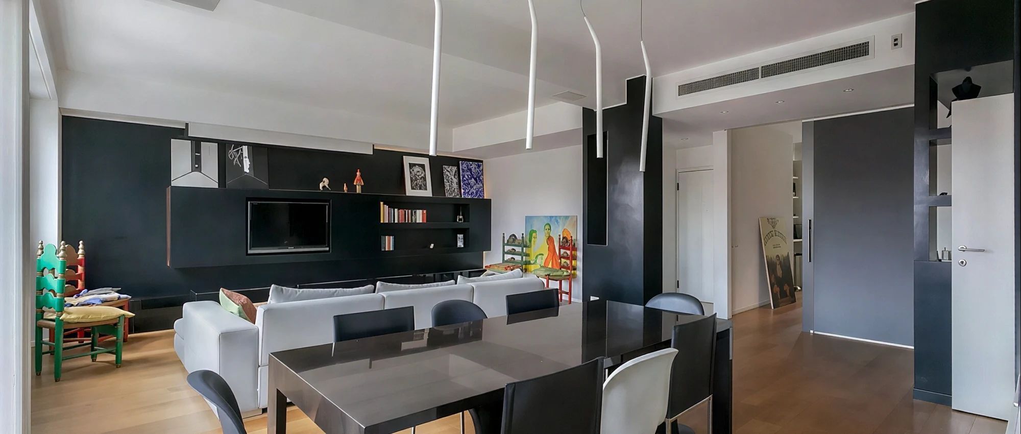 A modern dining area with a long table, chairs, and a black wall-mounted TV.