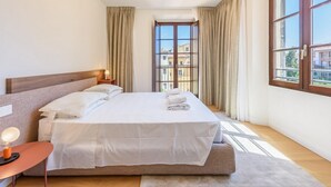 Une chambre d’hôtel avec un grand lit, une table de chevet avec une lampe, une fenêtre avec des rideaux et une vue sur les bâtiments environnants.