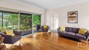 Amplia sala de estar con un gran ventanal corredizo que da a un patio, un sofá, dos sillones y un cuadro en la pared.