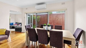 Un comedor moderno con una mesa y sillas de madera, un sofá y un ventanal corredera que da a un patio.