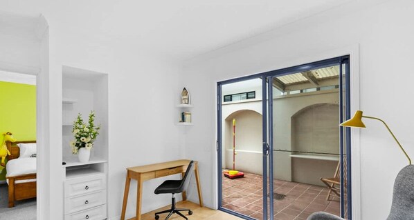 Ein Zimmer mit Schreibtisch, Stuhl und einer Glastür, die auf einen Balkon führt.