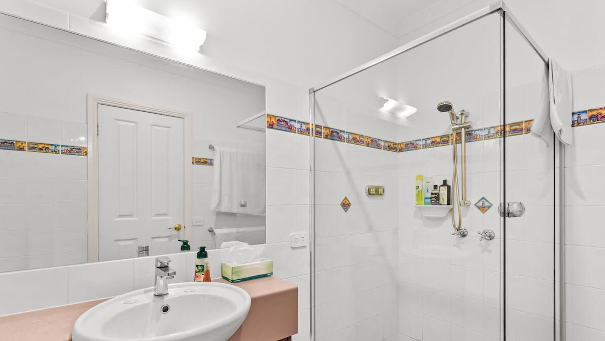 A bathroom with a sink, mirror, shower, and toiletries.