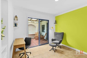 Ein modernes Zimmer mit einem Holztisch, zwei Stühlen, einer leuchtend grünen Akzentwand und einer Glastür, die auf eine Außenpatio führt.